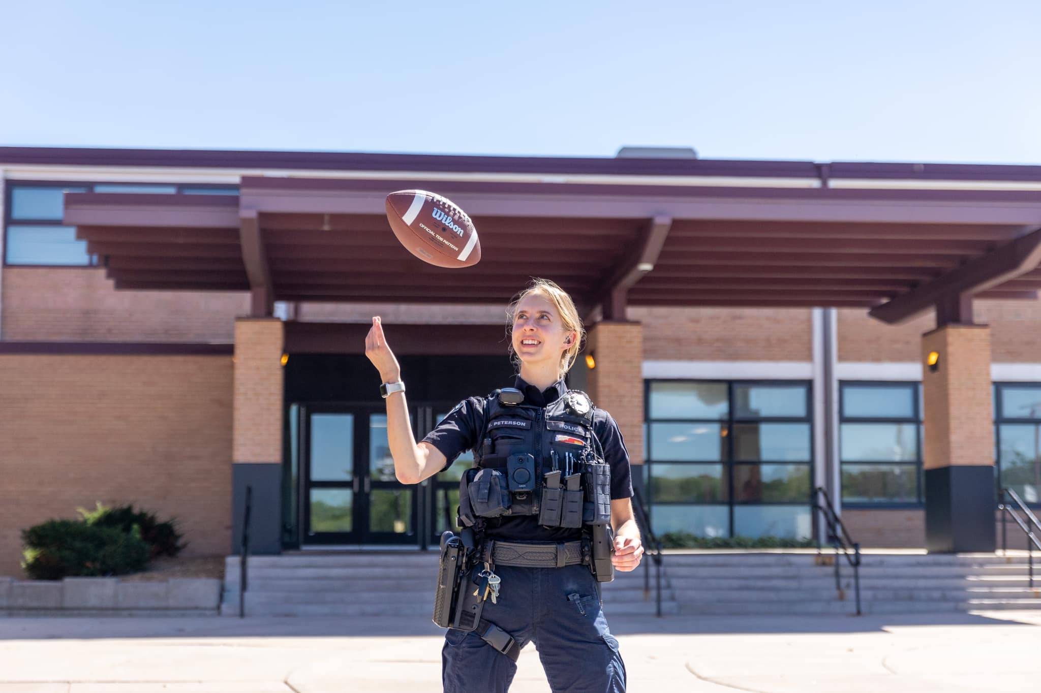 School Resource Officer Rieffer poses for a picture with a football in front of the school.