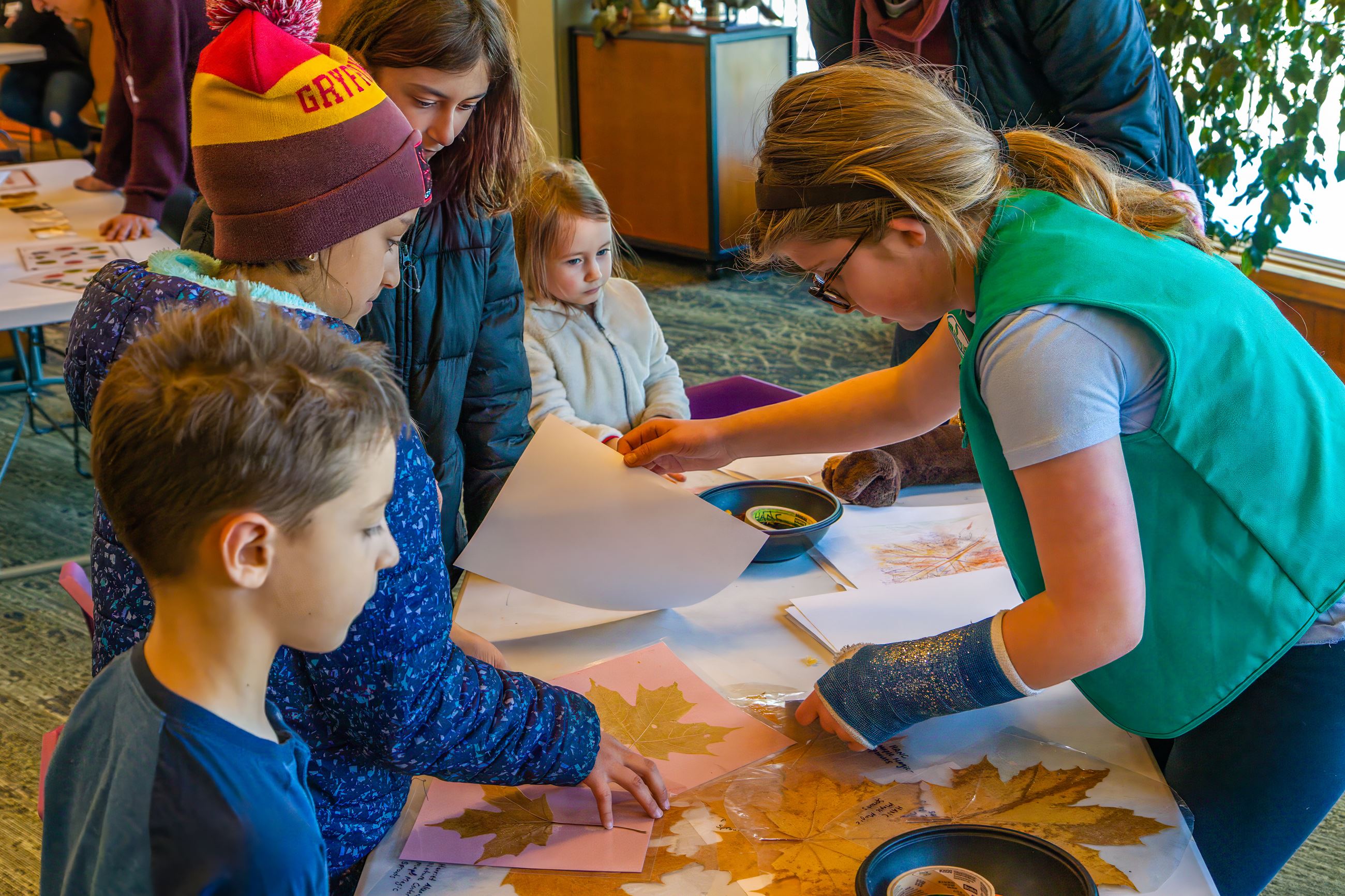 Girl Scout volunteer assisting children with leaf rubbing activity